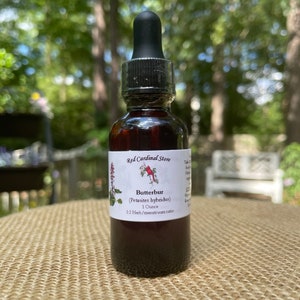 May include: A small brown glass bottle with a black dropper top. The bottle is labeled "Red Cardinal Store" and contains a dark liquid. The label also reads "Butterbur (Petasites hybridus) 1 Ounce 1:2 Herb/menstruum ratio".