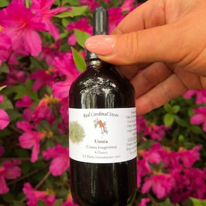May include: A dark glass bottle with a dropper, labeled "Red Cardinal Store" and "Usnea (Usnea longissima) 4 Ounce 1:2 Herb/menstruum ratio".