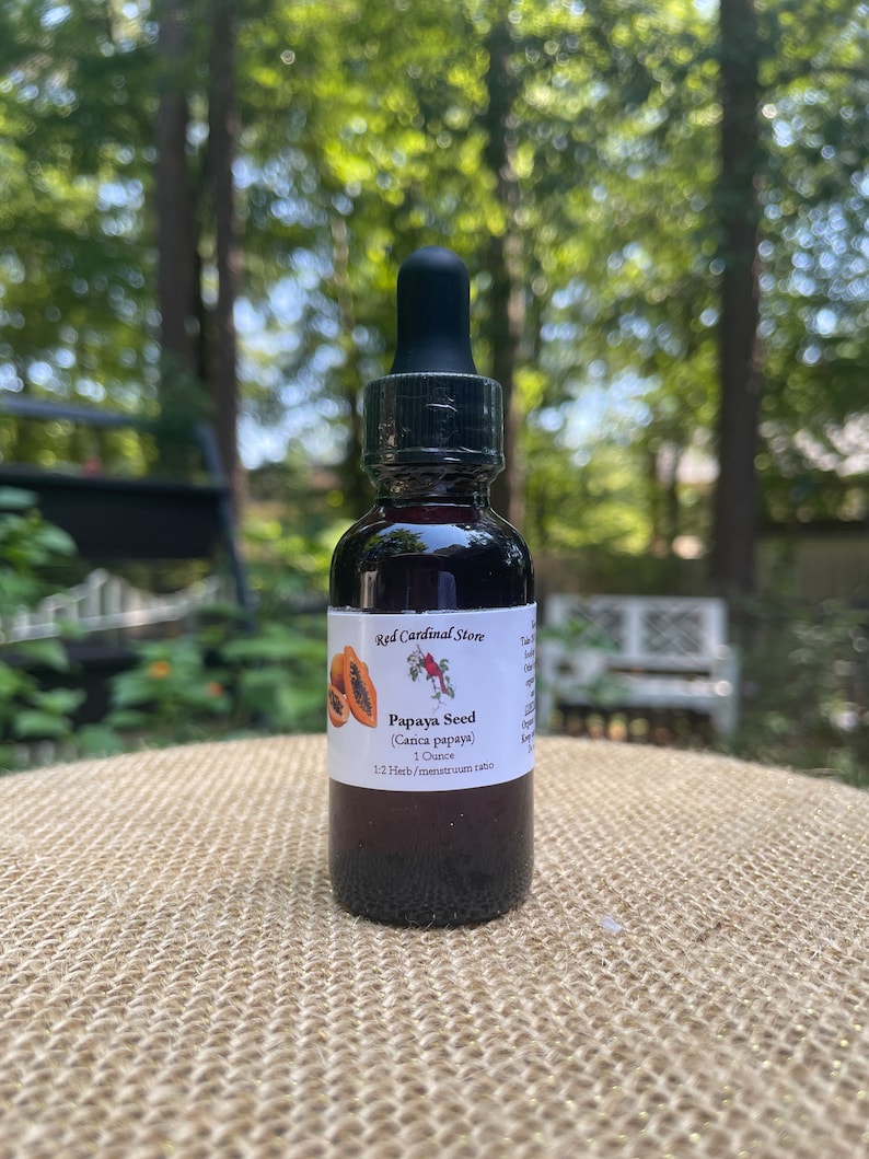 May include: A small, dark brown glass bottle with a black dropper top. The bottle is labelled "Red Cardinal Store Papaya Seed (Carica papaya) 1 Ounce 1:2 Herb/menstruam ratio".