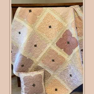 May include: A quilt pattern called "Sweet Pea" with a pink, white, and brown color scheme. The quilt is shown in three sizes: 60 inches by 60 inches, 45 inches by 45 inches, and 18 inches by 18 inches.
