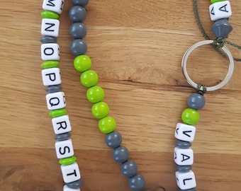 Könnte beinhalten: Eine graue und grüne Alphabet-Perlenkette mit einem Waschbär-Anhänger und einem Schlüsselring. Die Kette hat die Buchstaben A bis Z und die Zahlen 1 und 2.