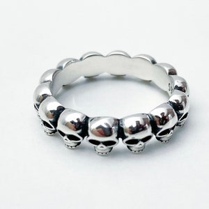 May include: Silver skull ring with a band of skulls around the entire ring.