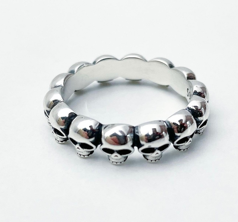 May include: Silver skull ring with a band of skulls around the entire ring.