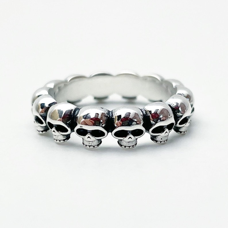 May include: A silver ring with a band of connected skull heads.