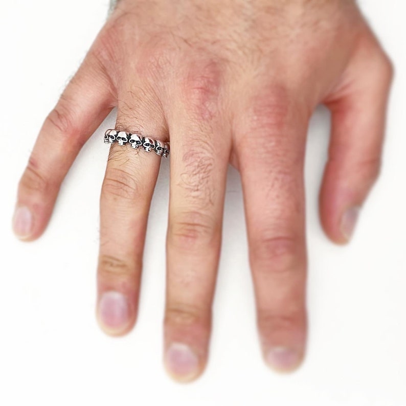 May include: A silver ring featuring a row of small skull designs.