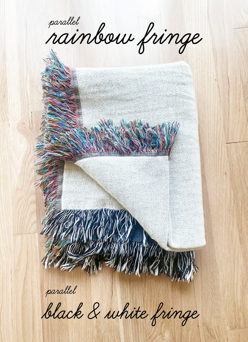 May include: A white throw blanket with two different fringe styles. One side has a rainbow fringe and the other side has a black and white fringe. The text "parallel rainbow fringe" is above the blanket and the text "parallel black & white fringe" is below the blanket.
