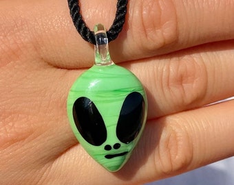 Peut inclure: Un pendentif en verre vert en forme d'extraterrestre avec des yeux noirs et un collier en cordon noir.