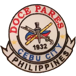 Puede incluir: Parche bordado con un diseño circular con el texto "Doce Pares" en rojo, "Cebu City Philippines" en azul y "1932". El diseño central incluye armas cruzadas y una bandera.
