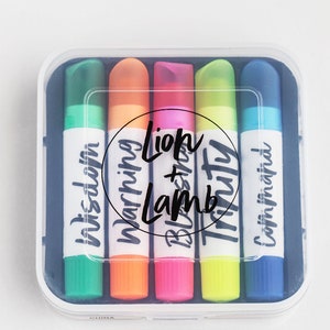May include: A set of six colorful highlighters in a clear plastic case. The highlighters are labeled with the words "In this dawn", "Morning", "Lion + Lamb", "Truth", and "Come in faith".