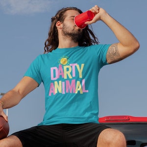 May include: A person wearing a turquoise blue t-shirt with the text "Party Animal" in pink and yellow letters, sitting on the back of a red pickup truck. The person is holding a football and a red cup.