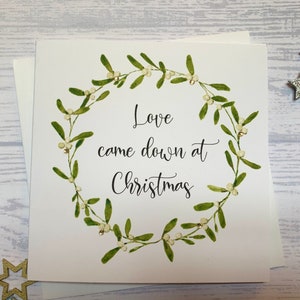 May include: A white card with a green mistletoe wreath and the text "Love came down at Christmas".