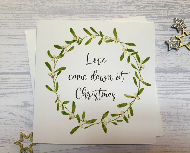 May include: A white card with a green mistletoe wreath and the text "Love came down at Christmas".