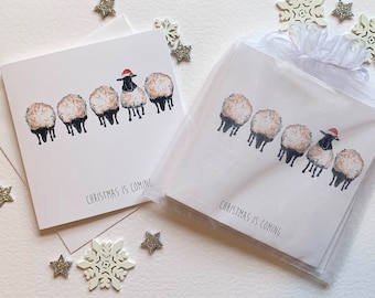 Cartes de Noël de luxe. Aquarelle de moutons mangeant de l'herbe avec un autre vers le haut portant un bonnet de Noel. Orné d'une pierre précieuse scintillante.