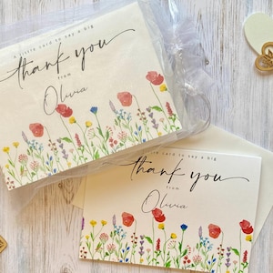 Peut inclure: Un ensemble de cartes de remerciement blanches avec une illustration aquarelle de fleurs sauvages colorées en bas. Le texte indique A little card to say a big thank you from Olivia. Les cartes sont emballées dans un sac en organza blanc.