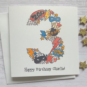 Superhero personalised 3rd  birthday card . Cartoon style watercolour illustration of the number 3 embellished with silver metallic detail.
