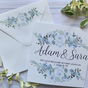 Carte de mariage chrétienne personnalisée avec des fleurs bleu pâle et des strass délicats. Nous aimons parce qu'il nous a aimés le premier. 1 Jean 4:19