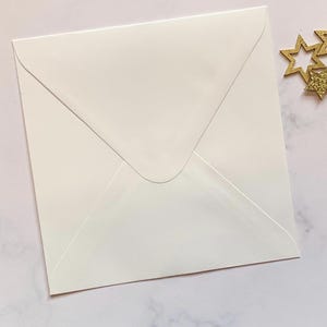 May include: A white envelope with a pointed flap. The envelope is lying flat on a light pink surface.