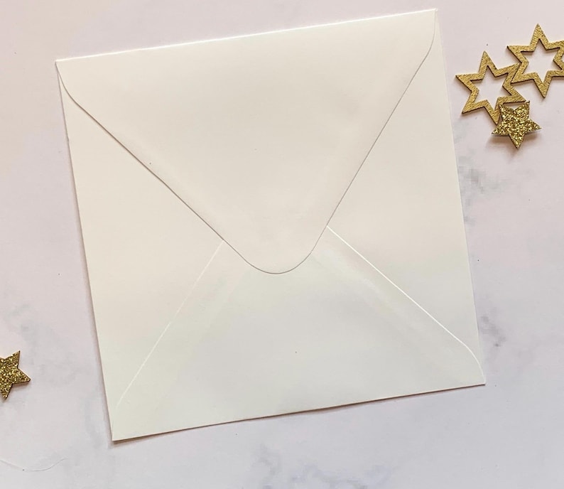 May include: A white envelope with a pointed flap. The envelope is lying flat on a light pink surface.