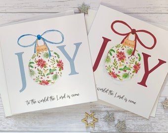 May include: Two Christmas cards with the word "JOY" in large, stylized letters. Each card features a watercolor illustration of a Christmas ornament with a floral pattern and a ribbon. The text "to the world the Lord is come" is printed on the bottom of each card.