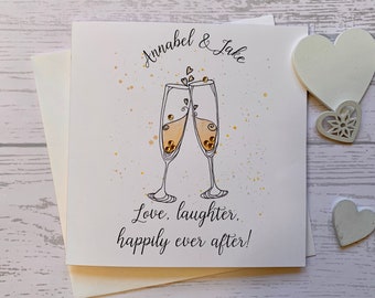 Carte de mariage personnalisée avec les mots « Amour, rire, bonheur pour toujours » imprimé sous deux coupes de champagne. Le nom du couple est au-dessus