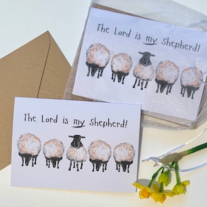 May include: A white card with the text "The Lord is my Shepherd!" and a row of five black and white sheep illustrations. The card is on a white background with a brown envelope and a bouquet of yellow daffodils.