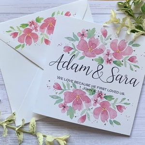 Carte de mariage chrétienne personnalisée avec des fleurs roses et des strass délicats. Nous aimons parce qu'il nous a aimés le premier. 1 Jean 4:19