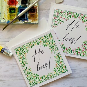 Emportez des cartes de Pâques chrétiennes.  Des fleurs délicates entourent les mots « Il vit ! ». Ornée de pierres précieuses. Cartes de luxe. Cartes confessionnelles