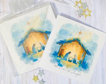 May include: White handkerchief and card set featuring a watercolor illustration of a nativity scene with a star. The text "All is calm all is bright" is printed on the card. Includes gold and silver star-shaped decorations.