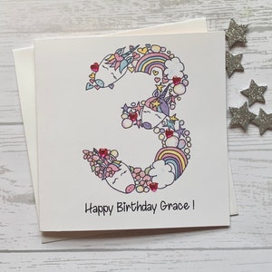 Unicorn personalised 3rd   birthday card . Cartoon/doodle  style watercolour illustration of the number 3 embellished with heart gems..