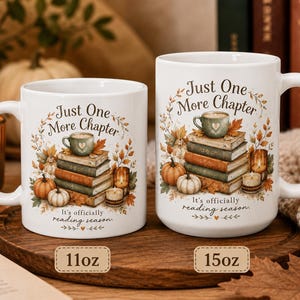 May include: Two white ceramic mugs, one 11oz and one 15oz, featuring a printed illustration of a stack of books, pumpkins, candles, and autumn leaves. The text reads Just One More Chapter and It's officially reading season in a dark script font.
