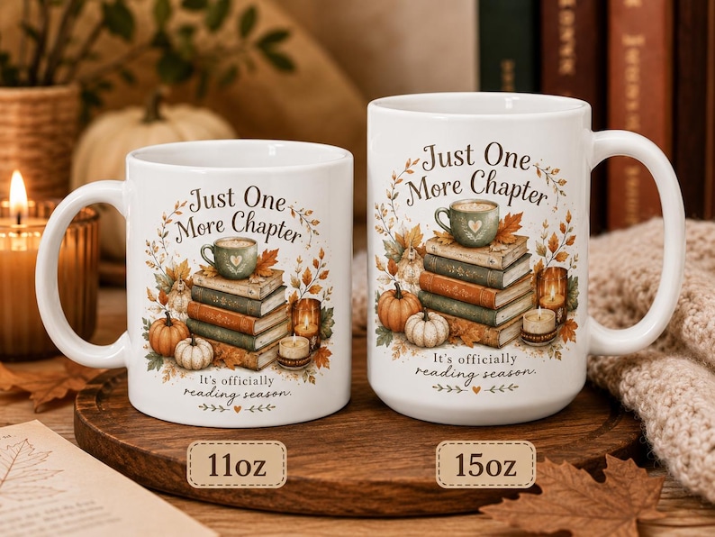 May include: Two white ceramic mugs, one 11oz and one 15oz, featuring a printed illustration of a stack of books, pumpkins, candles, and autumn leaves. The text reads Just One More Chapter and It's officially reading season in a dark script font.