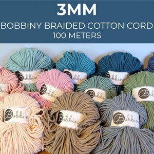 May include: Multiple skeins of 3mm Bobbiny braided cotton cord, each 100 meters long. The collection features various colors including light pink, dusty rose, sage green, teal, dark blue, and gray, all with white labels marked with the Bobbiny logo.