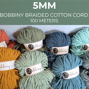 May include: A collection of 5mm Bobbiny braided cotton cord spools, each 100 meters long. The yarn is available in various colors including terracotta, mustard yellow, sage green, dark blue, teal, and light blue, all featuring white labels.