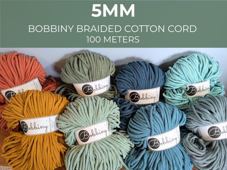 May include: A collection of 5mm Bobbiny braided cotton cord spools, each 100 meters long. The yarn is available in various colors including terracotta, mustard yellow, sage green, dark blue, teal, and light blue, all featuring white labels.