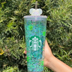 May include: A clear plastic tumbler with a green glitter design and a white heart-shaped lid with rhinestones. The tumbler features a green Starbucks logo and a green Yoda character.