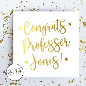 May include: A white card with gold foil lettering reading "Congrats Professor Jones!" with star accents. Gold confetti surrounds the card, which has a "Real Foil" logo.