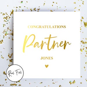 May include: White card with gold foil lettering. The card says "Congratulations Partner JONES" with a small gold heart at the bottom.