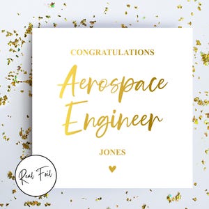 May include: A white card with gold foil lettering saying "CONGRATULATIONS Aerospace Engineer" and the name "JONES". A small gold heart is below the name. Gold confetti surrounds the card.