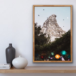 Pu&ograve; includere: Una fotografia incorniciata di una montagna con una cima innevata, circondata da alberi e un cielo blu. Ci sono diversi uccelli che volano nel cielo. La montagna &egrave; illuminata da luci colorate alla base.
