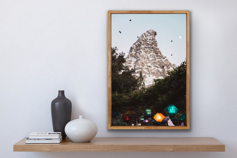 Pu&ograve; includere: Una fotografia incorniciata di una montagna con una cima innevata, circondata da alberi e un cielo blu. Ci sono diversi uccelli che volano nel cielo. La montagna &egrave; illuminata da luci colorate alla base.