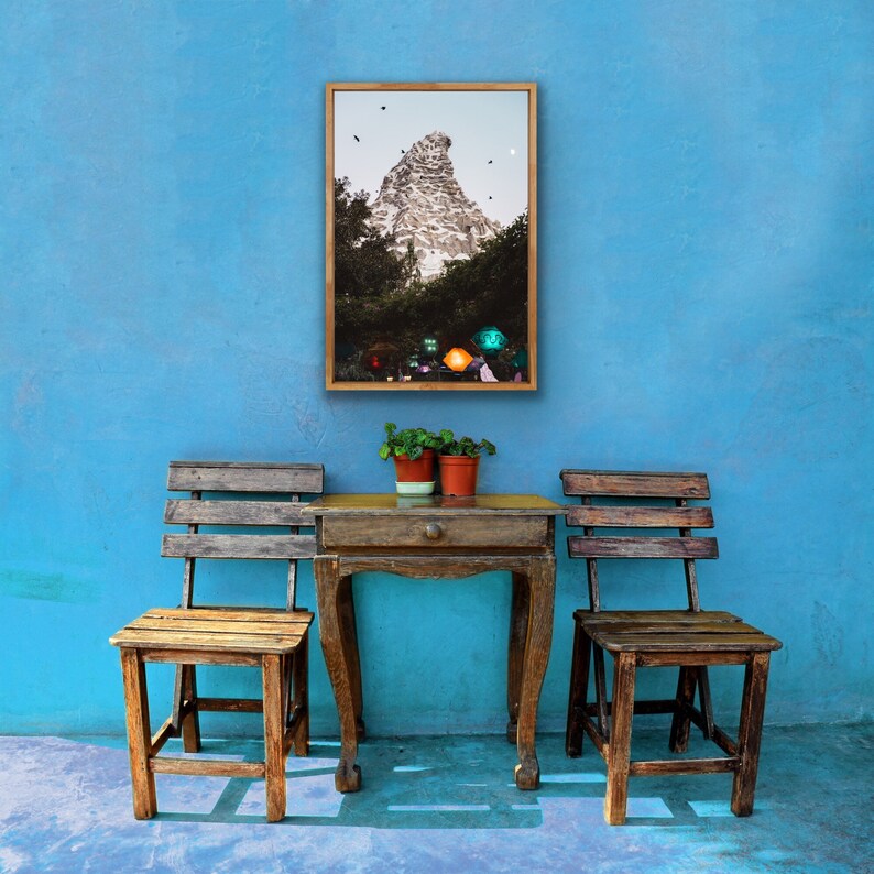 Pu&ograve; includere: Due sedie di legno con un tavolo di legno davanti a un muro blu. Un quadro incorniciato di una montagna con un edificio in cima &egrave; appeso al muro.