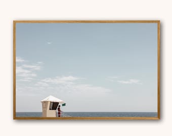 May include: A white lifeguard stand with a red roof on a beach with a blue sky and ocean in the background.