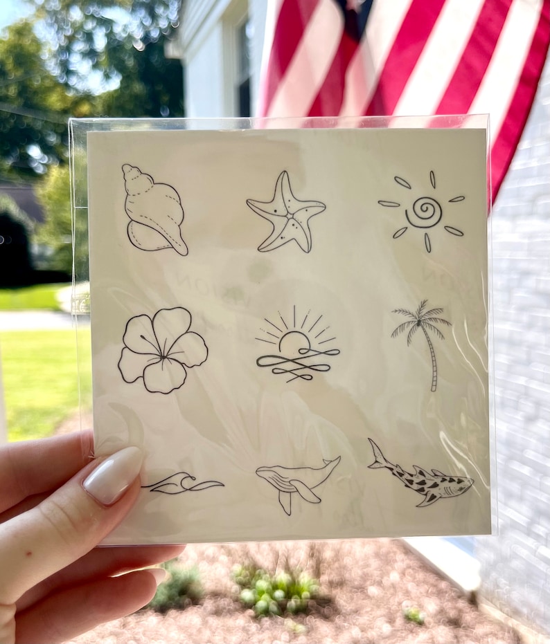 May include: A sheet of temporary tattoos with nine different designs, including a seashell, starfish, sun, hibiscus flower, sunrise, palm tree, wave, whale, and shark. The tattoos are black and white.