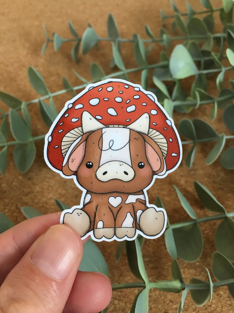 May include: A cartoon cow wearing a red and white mushroom hat. The cow is brown with white spots and has a heart-shaped spot on its side. The mushroom has white dots on a red background.