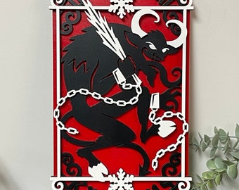 May include: A red wooden sign with a white silhouette of a horned creature chained and holding a whip. The sign reads "Gruss vom Krampus" in black lettering.
