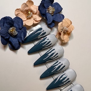 以下が含まれることがあります： 白とターコイズブルーのグラデーションデザインが施された、長い人工爪のセットです。爪は透明なプラスチック製のディスプレイカードに並べてあります。