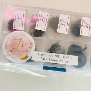 May include: A clear plastic container with 6 compartments, each containing a small bundle of black eyelash extensions. The container has a label that reads "Handmade 20D / 0.03D MIX 16mm-20mm".