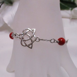 May include: Silver Celtic knot charm bracelet with two red beads.