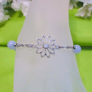 May include: A silver chain bracelet with a delicate flower charm and two light blue beads.