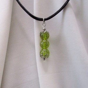 May include: A green gemstone necklace with three round beads on a black cord.
